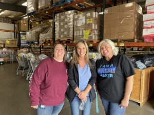 Three women pose together in warehouse at volunteer event