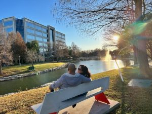 Lao and Tom sit on a bench by a lake looking at our Dallas office