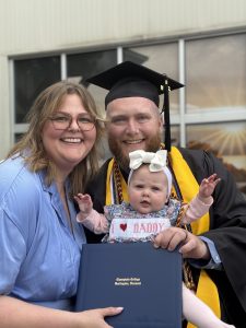 Blake in graduation cap and gown with his wife and child