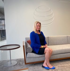 Cher in business attire sits beneath AT&T logo sign