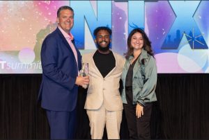 Two men and woman in business casual attire pose for a photo with the Summit award