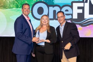 Two men and woman in business casual attire pose for a photo with the Summit award